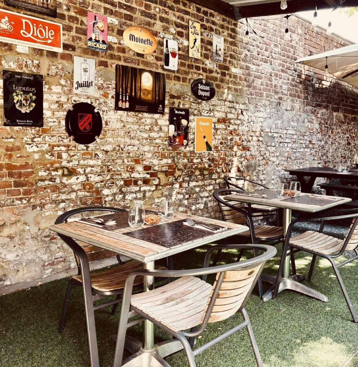 Tables de la terrasse devant le mur de briques tapissé de plaques émaillées de bières belges